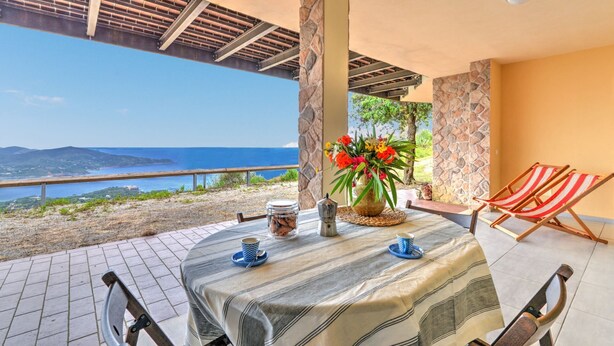 A table set for two with a view of the sea, a stone pillar, and a chair.