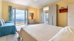A bedroom with a large bed, a dresser, and a view of the sea.