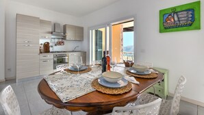 A dining area with a wooden table set for four, a kitchen in the background, and a view of the outdoors.