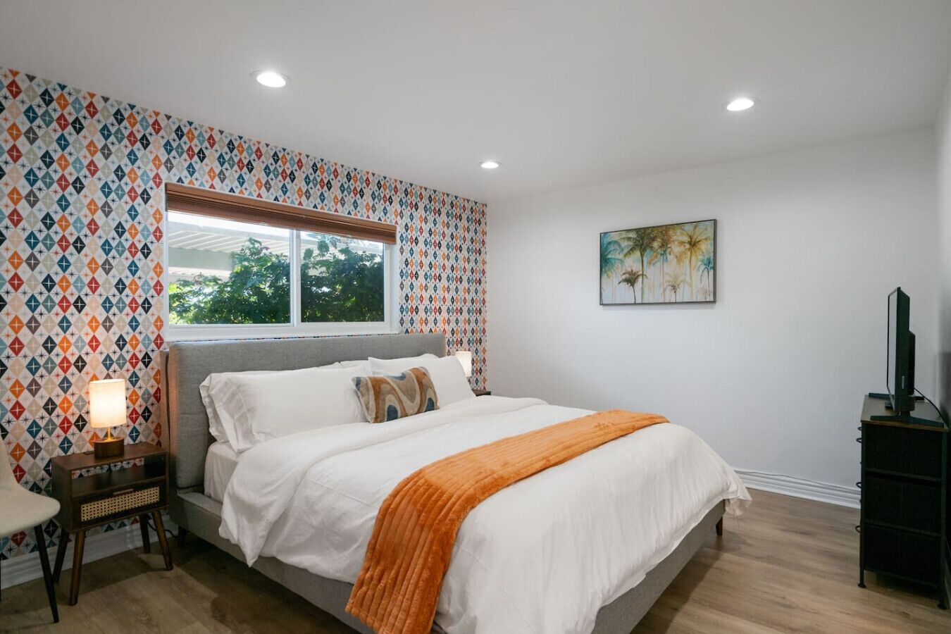 A bedroom with a bed, a window, a painting, and a TV stand.