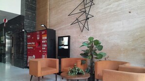 A lobby with orange armchairs, a coffee table, a large potted plant, a PopBox vending machine, and a security camera. - Roket Room Majestic Point (Gading Serpong)