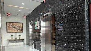 A modern lobby with a marble wall, a bench with plants, and an elevator. - Roket Room Majestic Point (Gading Serpong)