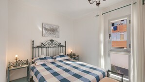Un dormitorio con cama, mesita de noche, ventana con vistas y candelabro.