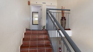 Una escalera con barandilla de metal, un extintor y una planta en maceta.