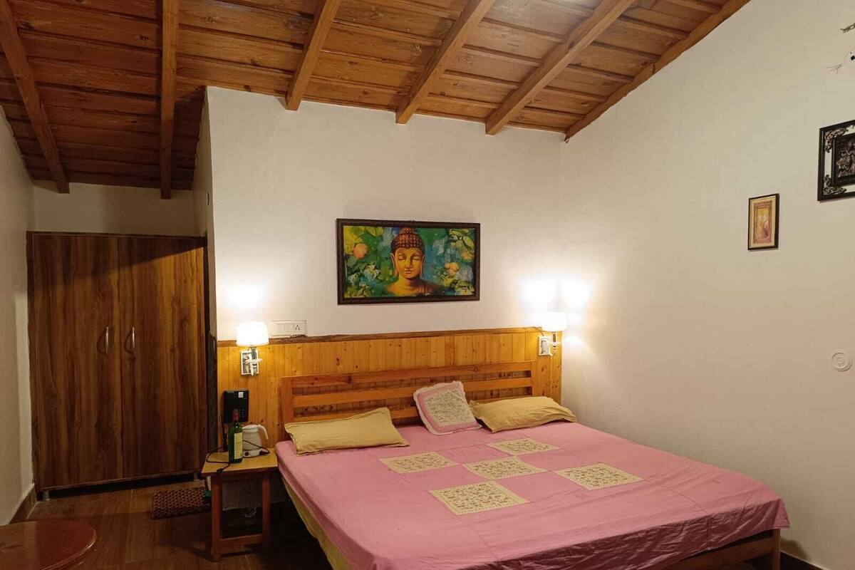 Un dormitorio con techo de madera, una cama con colcha rosa, dos lámparas de noche, un armario de madera y un cuadro en la pared.