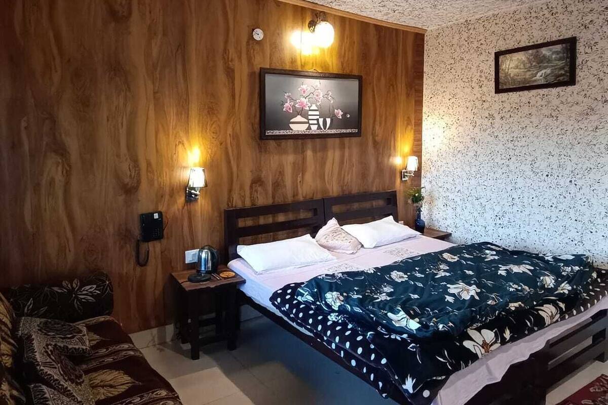 Un dormitorio con cabecera de madera, cama con colcha floral, dos lámparas de noche, mesita de noche con teléfono y un cuadro enmarcado en la pared.