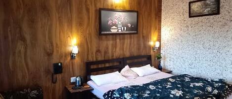 A bedroom with a wooden headboard, a bed with a floral bedspread, two bedside lamps, a nightstand with a phone, and a framed picture on the wall.