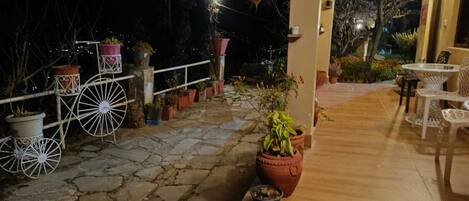 A patio area with stone flooring, white metal chairs, and potted plants.