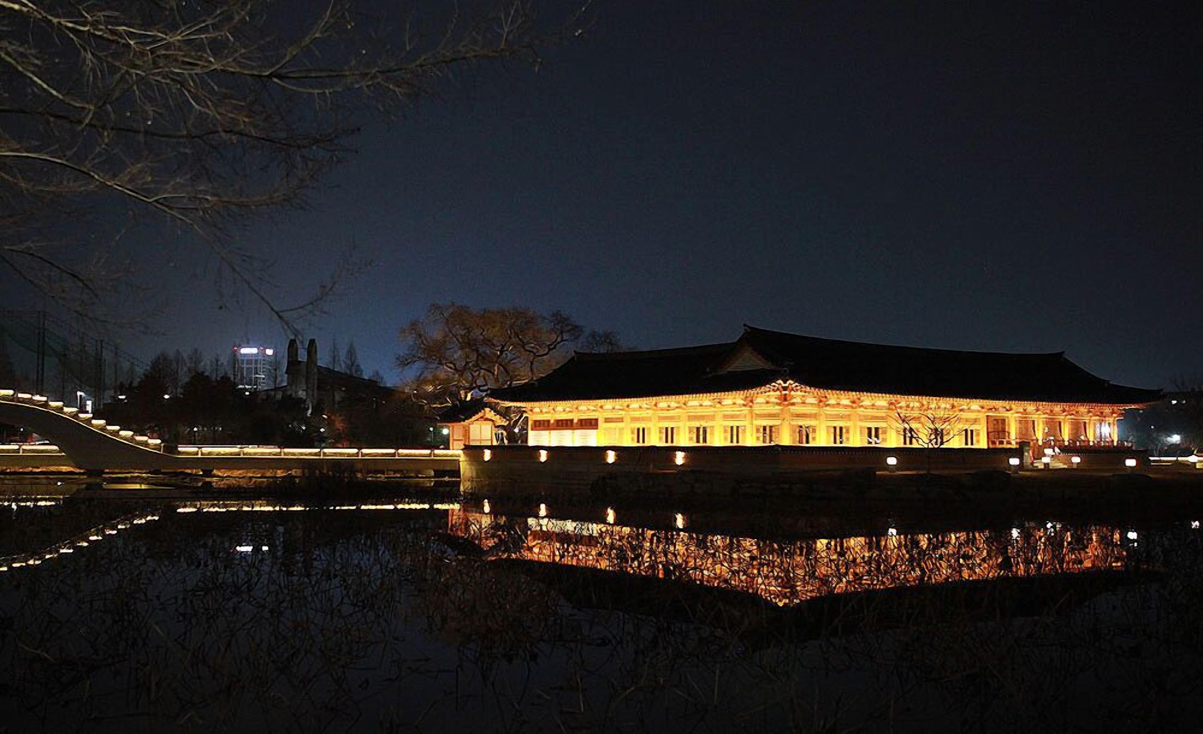 A traditional building with a reflection in the water, a bridge, and a tree in the background.