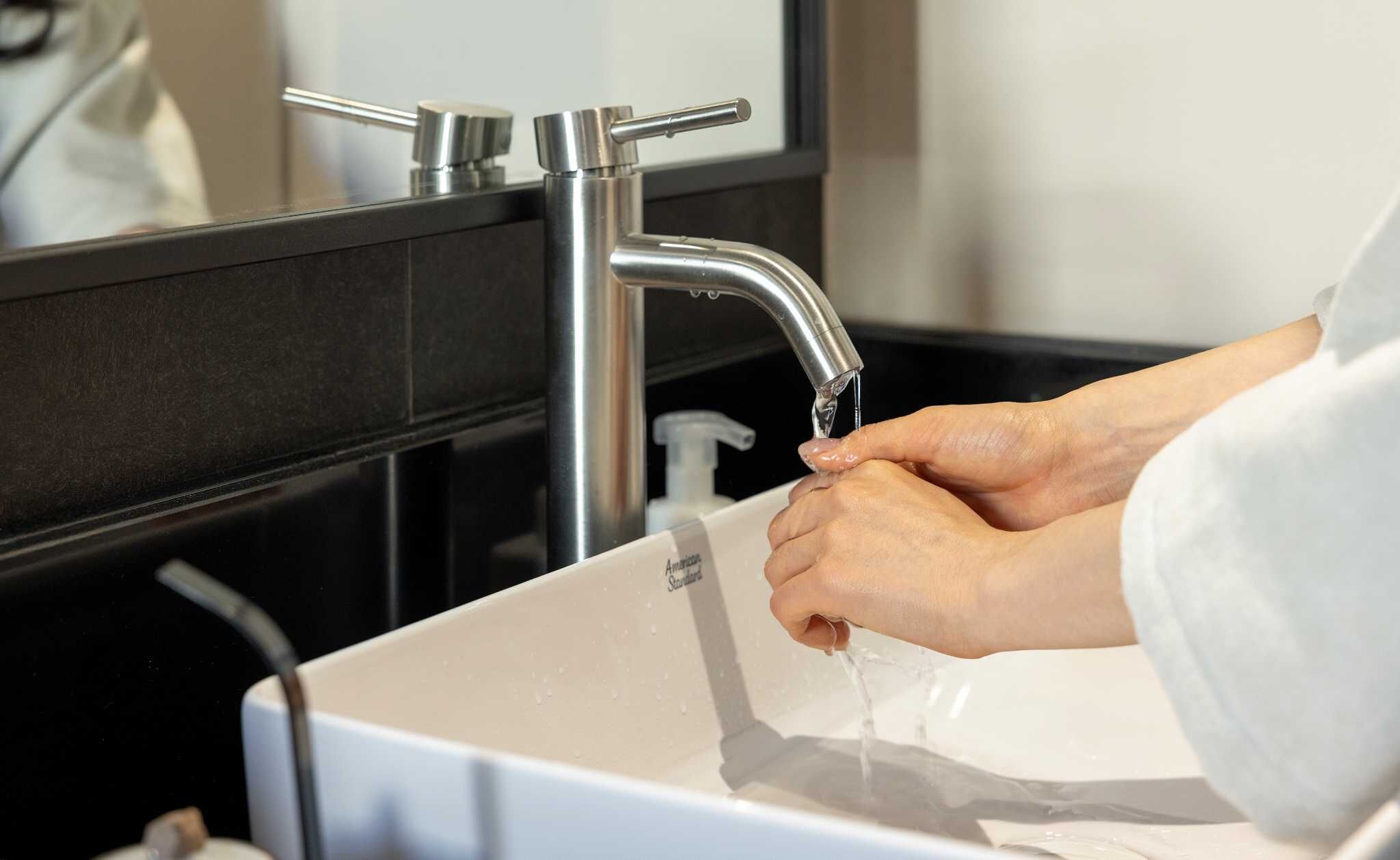 A person washing hands in a modern bathroom with a white sink and a black countertop.