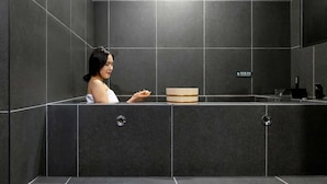Un baño moderno con azulejos oscuros, un lavamanos y un letrero de precaución.