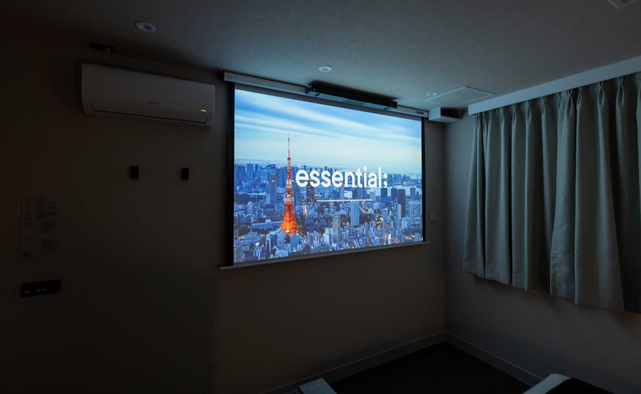A projection screen in a room with a cityscape view, air conditioning unit, and curtains.