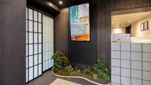 Una zona de recepción con un mostrador de madera, un cartel grande y un pequeño jardín interior.