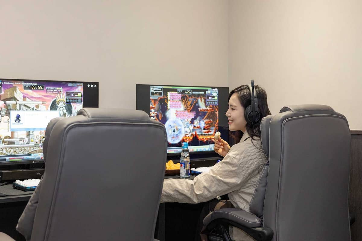 Una persona jugando videojuegos en un escritorio con dos monitores, un teclado y una botella de agua.