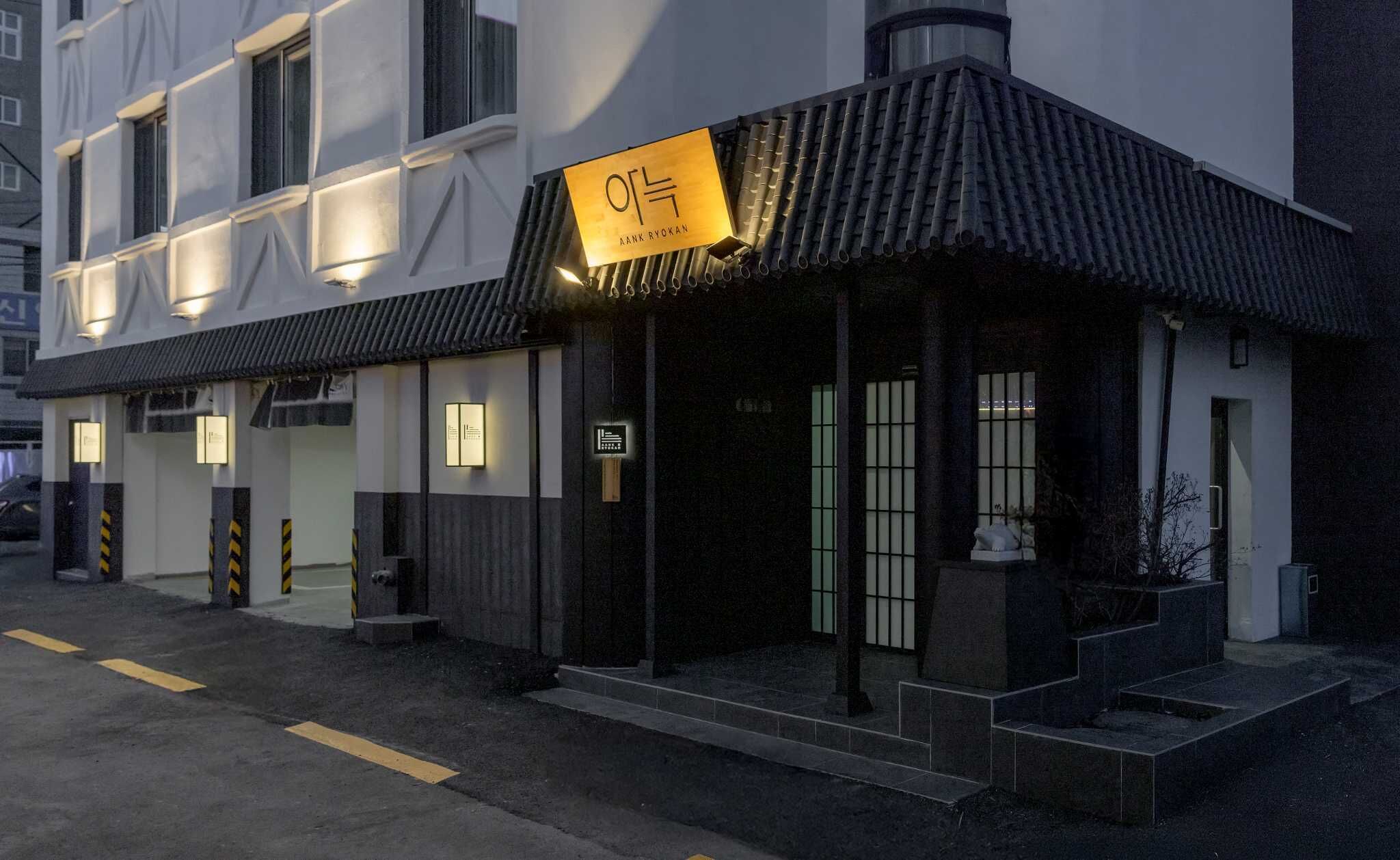A building with a modern facade, a sign reading "AANK RYOKAN," and a traditional tiled roof.