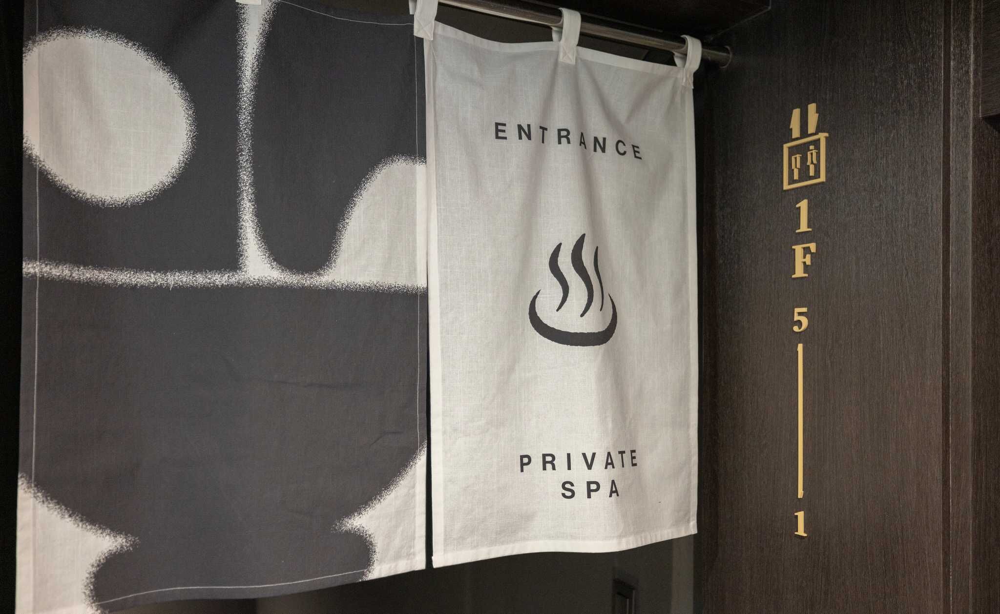 Entrada privada a un spa, con una toalla colgada en un gancho, un cartel que indica 'ENTRANCE' y 'SPA PRIVADO', y una pared con el número '1F 5 1'.