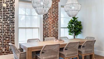 A dining area with a brick wall, large windows, wicker chairs, and a wooden table.