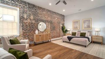 A modern bedroom with a brick wall, a round mirror, a bed with pillows, a nightstand, and a chair.
