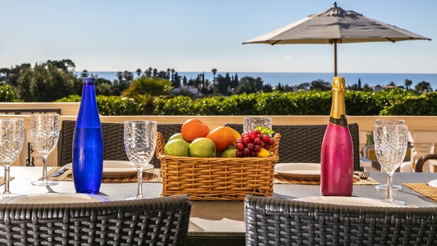 A table set with a fruit basket, a champagne bottle, and empty wine glasses, overlooking a scenic view. - Casa Jean - Private villa with sea view and heatable pool (Carvoeiro)