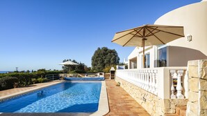 A swimming pool with a stone wall and a white building with a balcony. - Casa Jean - Private villa with sea view and heatable pool (Carvoeiro)