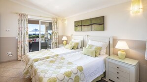 A bedroom with two beds, a glass door leading to a balcony, and a painting on the wall. - Casa Jean - Private villa with sea view and heatable pool (Carvoeiro)
