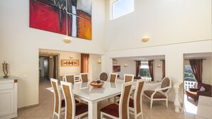 A spacious dining area with a glass table and wicker chairs, a modern abstract painting, and a view of the outdoors. - Casa Jean - Private villa with sea view and heatable pool (Carvoeiro)