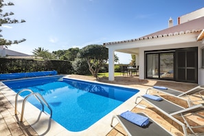 Ein Schwimmbecken mit Metallleiter, Liegestühlen und einem überdachten Patio.