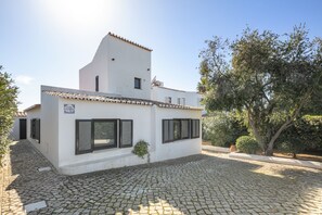 Un bâtiment blanc avec un toit en tuiles, une cour pavée et un arbre.