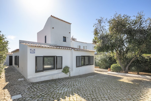 A white building with a tiled roof, a cobblestone courtyard, and a tree.