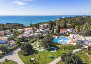 Vue aérienne d’un quartier résidentiel situé sur la côte, avec des maisons, une piscine et un phare visible au loin.