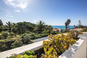 A coastal landscape with a view of the sea, surrounded by lush greenery and palm trees.
