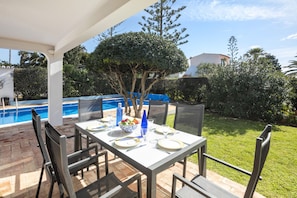 An outdoor dining area with a table set for four, surrounded by chairs, near a pool and garden.