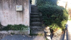 A residential building with a concrete wall, a small utility box, and a set of stone steps leading to a door. - Vacation rental 4 people arrière pays grassois (Cabris)
