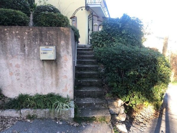 A residential building with a concrete wall, a small utility box, and a set of stone steps leading to a door.