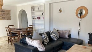 A modern living room with a black leather sofa, a wooden coffee table, and a dining area with a wooden table and chairs. - Vacation rental 4 people arrière pays grassois (Cabris)