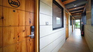 Un couloir aux murs recouverts de lambris en bois, une porte portant l’inscription « 205 », et un extincteur sur le côté droit.