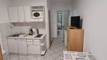 Una cocina compacta con armarios blancos, un microondas, una cafetera y una mesa con mantel estampado.