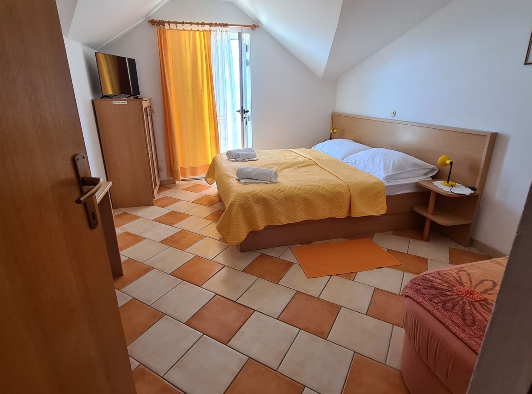 A bedroom with a bed, a nightstand, a lamp, a TV, and a wardrobe.