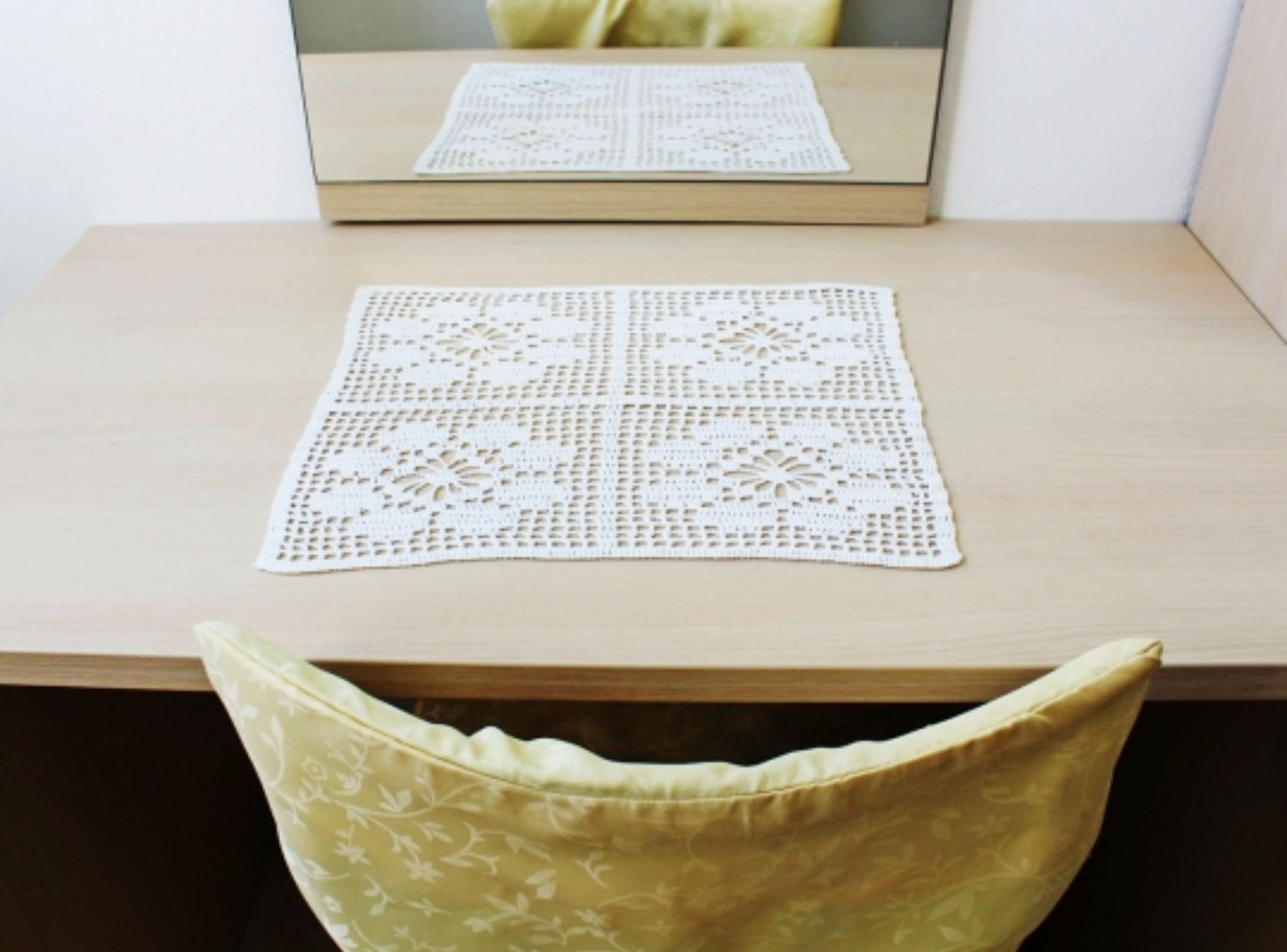 A wooden table with a white crocheted table runner and a mirror reflecting the table runner.