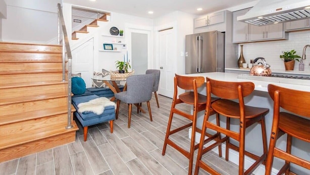 Una cocina moderna con una isla central, sillas de madera y una escalera que lleva a otra habitación.