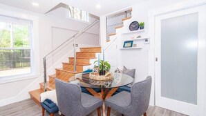 Un interior moderno con una mesa de comedor de cristal, sillas tapizadas de color gris, una escalera de madera y una puerta blanca.