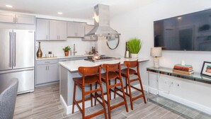 Una cocina moderna con una isla grande, taburetes de bar, una estufa empotrada y un televisor de pantalla plana montado en la pared.