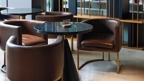A modern interior with a black and gold color scheme, featuring a round table, leather chairs, and a bookshelf with decorative items. - Aomori Hotel (Foshan)