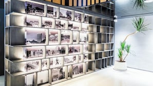A wall with a grid of framed photographs, a potted plant, and a wooden panel design. - Aomori Hotel (Foshan)