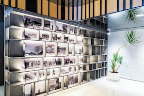 A wall with a grid of framed photographs, a potted plant, and a wooden panel design. - Aomori Hotel (Foshan)