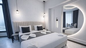 Une chambre d’hôtel moderne dotée d’un grand lit, de tables de chevet, d’un miroir et d’un coin salon avec une table et des chaises.