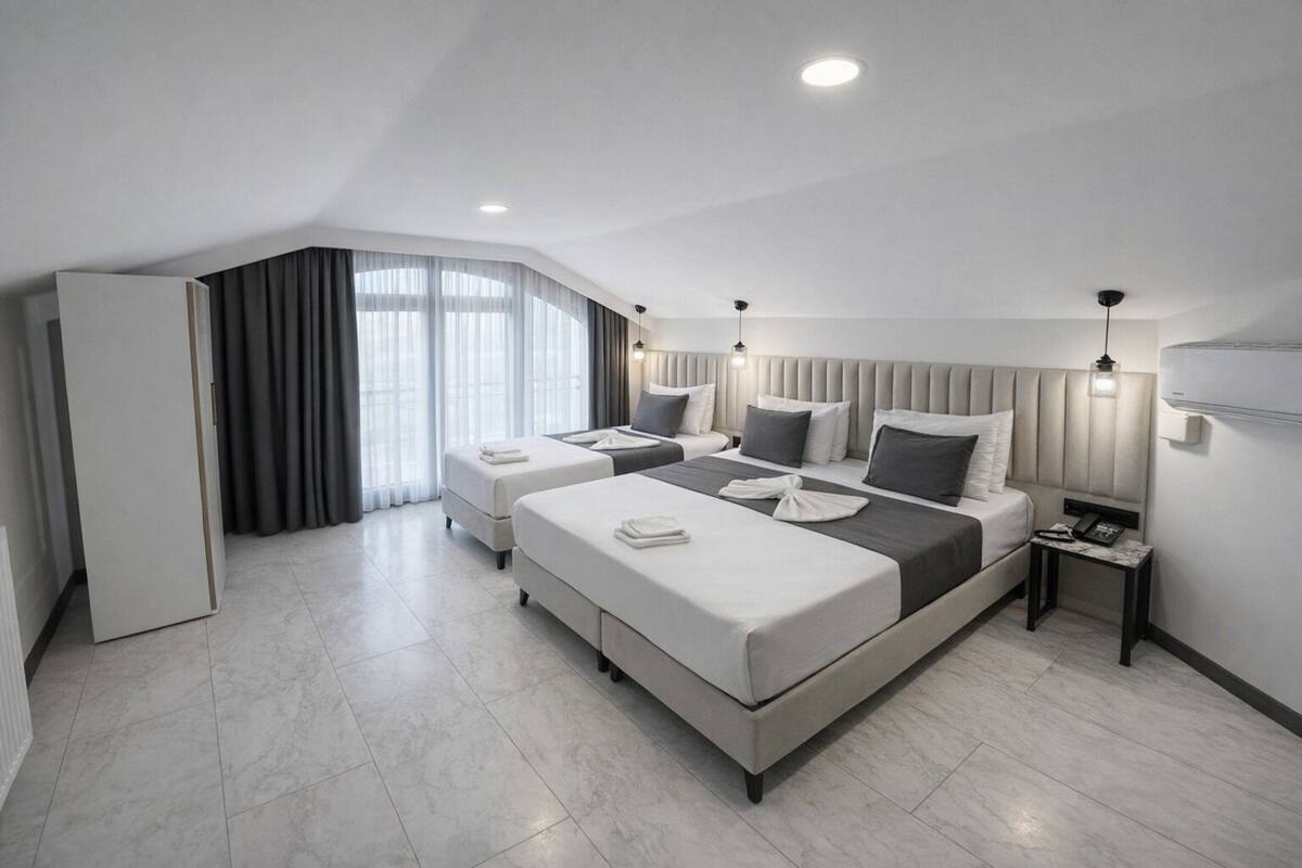Una habitación de hotel moderna con una cama grande, dos mesitas de noche, un armario y un ventanal con cortinas.