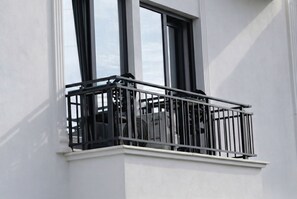 Un balcon avec une balustrade en métal, un mur blanc et une fenêtre.