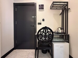 A room with a closed door, a chair, a small table with a kettle, and a refrigerator. - D Twins plus Hotel (Arnavutköy)