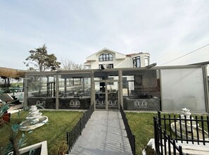 A modern house with a glass conservatory, a lawn, and a white building in the background. - D Twins plus Hotel (Arnavutköy)